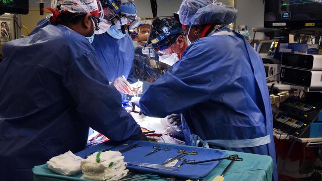 Ärzte in blauen Kitteln beugen sich über einen OP-Tisch im Krankenhaus. 