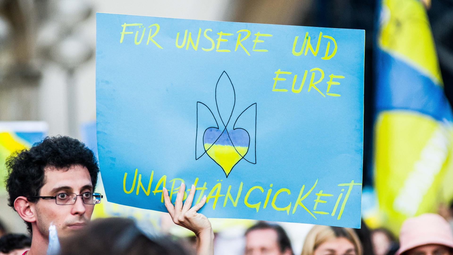 Ukrainische Geflüchtete und Unterstützerinnen und Unterstützer demonstrieren am Tag der Unabhängigkeit in München - auf einem Plakat steht "Für unsere und eure Unabhängigkeit", darauf auch das mit einem Herzen abgewandelte Zeichen des ukranischen Militärs