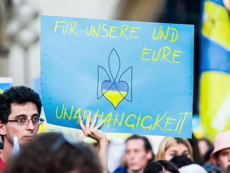 Ukrainische Geflüchtete und Unterstützerinnen und Unterstützer demonstrieren am Tag der Unabhängigkeit in München - auf einem Plakat steht "Für unsere und eure Unabhängigkeit", darauf auch das mit einem Herzen abgewandelte Zeichen des ukranischen Militärs