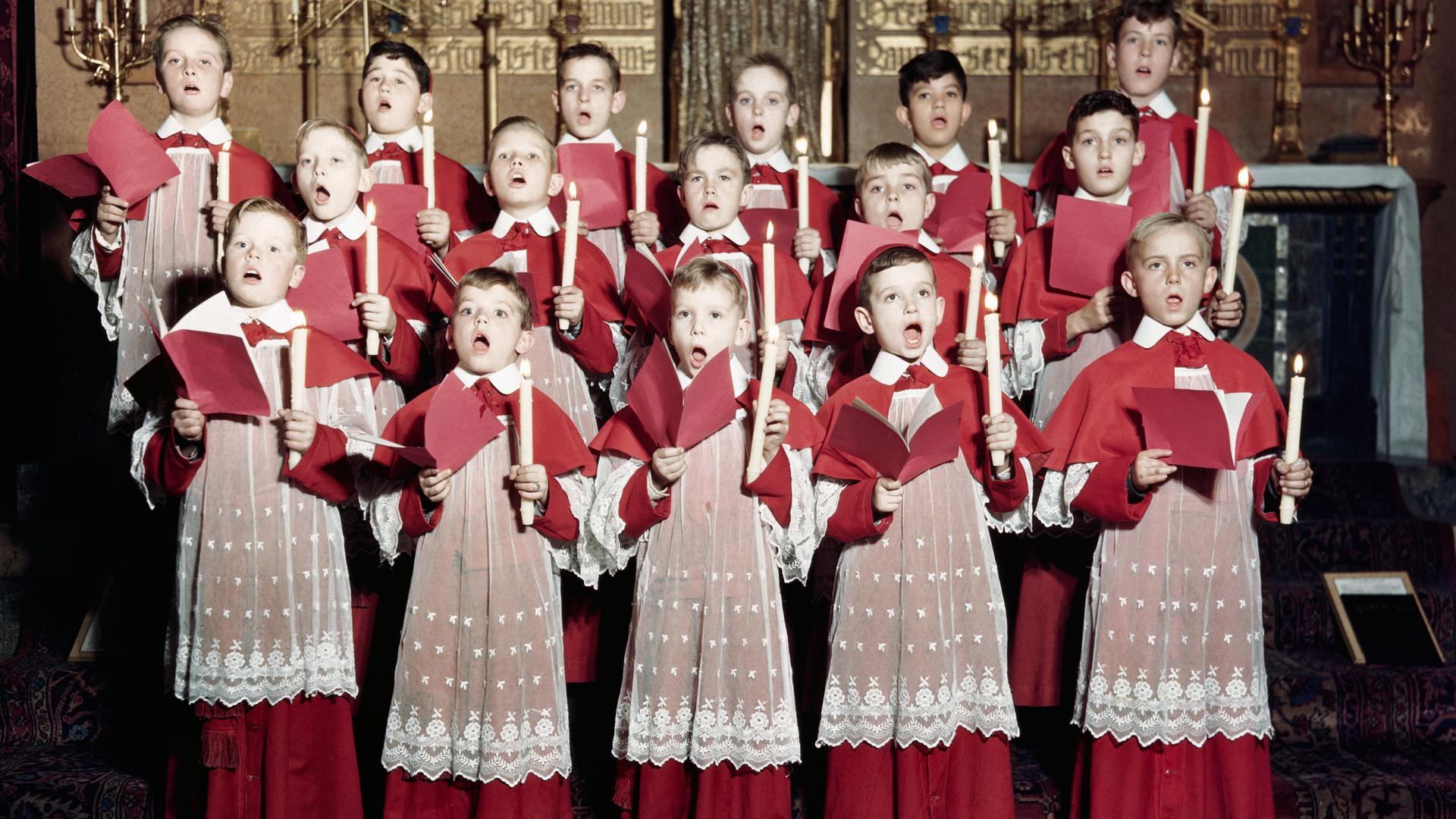 Jungs halten Kerzen und Notenblätter in den Händen und singen in einer Kirche. Jungs halten Kerzen und Notenblätter in den Händen und singen in einer Kirche.