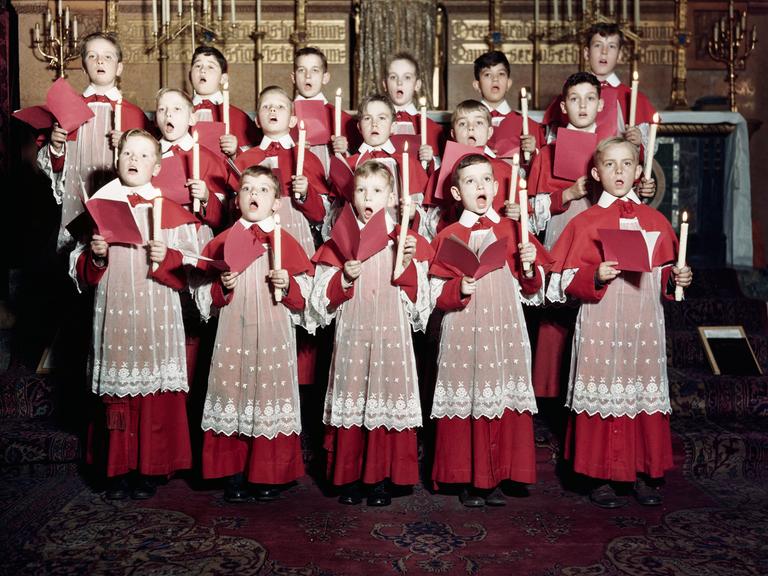 Jungs halten Kerzen und Notenblätter in den Händen und singen in einer Kirche.