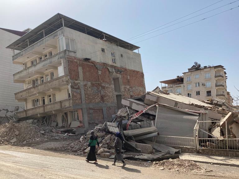 Zwei Frauen gehen auf einer Straße an zerstörten Häusern im türkischen Ort Kirikhan nahe der syrischen Grenze vorbei, knapp einen Monat nach den schweren Erdbeben.