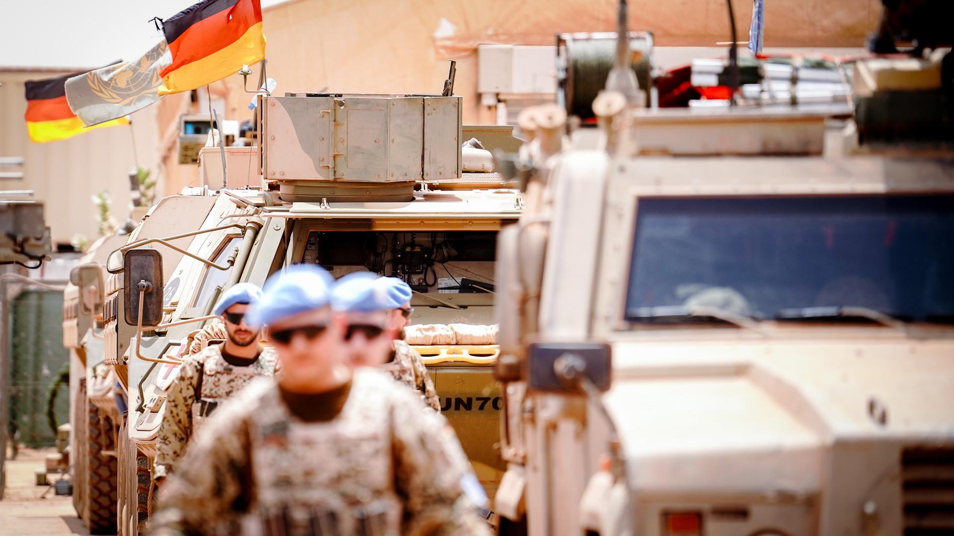 Die Deutschlandfahne und die Flagge der Vereinten Nationen wehen im Camp Castor in Gao, im Vordergrund sind Soldaten und gepanzerte Fahrzeuge zu sehen. Die Deutschlandfahne und die Flagge der Vereinten Nationen wehen im Camp Castor in Gao, im Vordergrund sind Soldaten und gepanzerte Fahrzeuge zu sehen.
