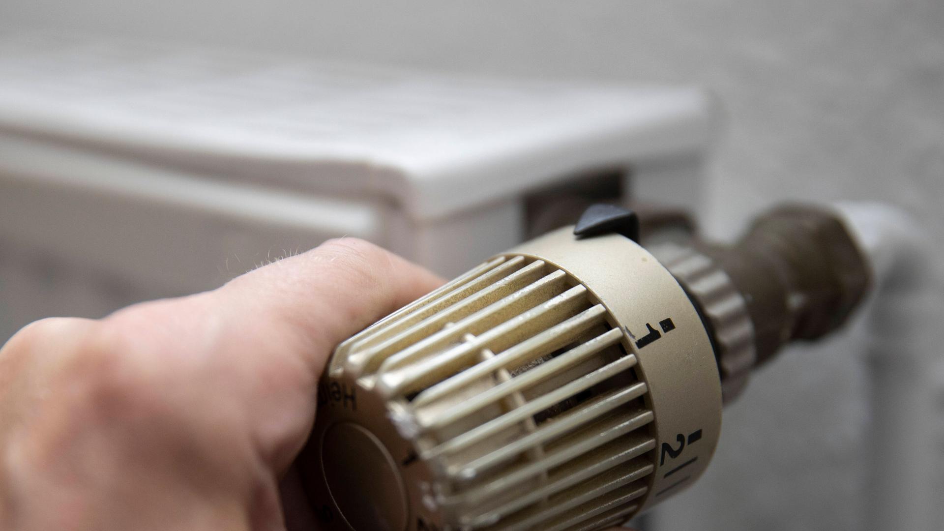 Eine Hand dreht an dem Thermostat von einem Heiz-Körper. Eine Hand dreht an dem Thermostat von einem Heiz-Körper.