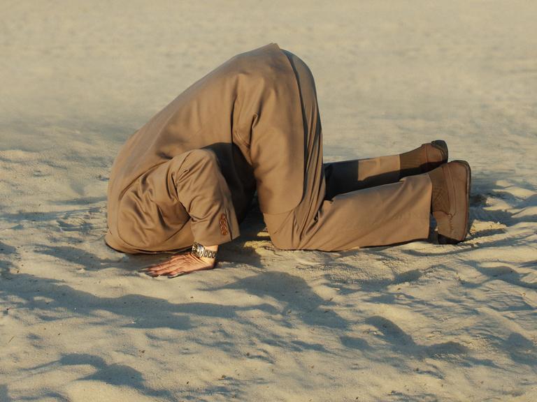 Geschäftsmann steckt seinen Kopf in Sand am Strand.