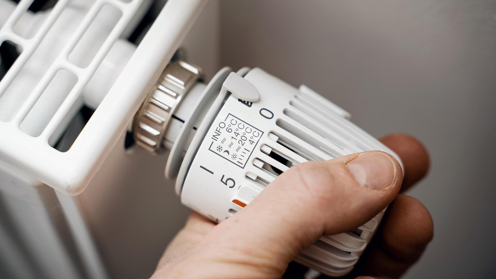 Eine Hand dreht den Thermostat einer Heizung auf Null. Eine Hand dreht den Thermostat einer Heizung auf Null.