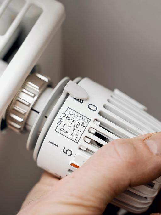 Eine Hand dreht den Thermostat einer Heizung auf Null.