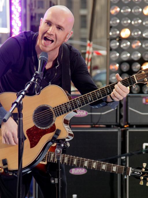 Der Gitarrist Mark Sheehan von "The Script" hat zwei Gitarren gleichzeitig umgehängt. Auf einer spielt er und singt dabei in ein Mikrofon.