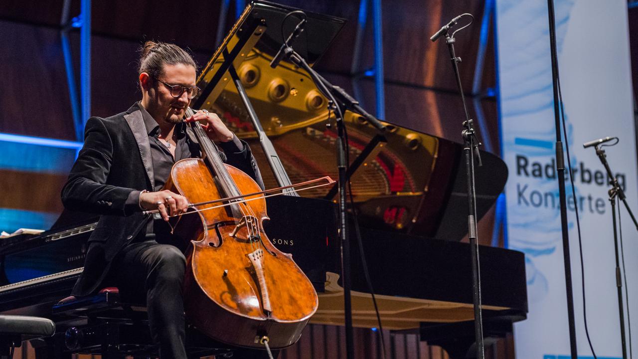 Santiago Cañón-Valencia sitzt mit seinem Violoncello auf der Bühne und spielt beim Raderbergkonzert ein Solowerk. Santiago Cañón-Valencia sitzt mit seinem Violoncello auf der Bühne und spielt beim Raderbergkonzert ein Solowerk.