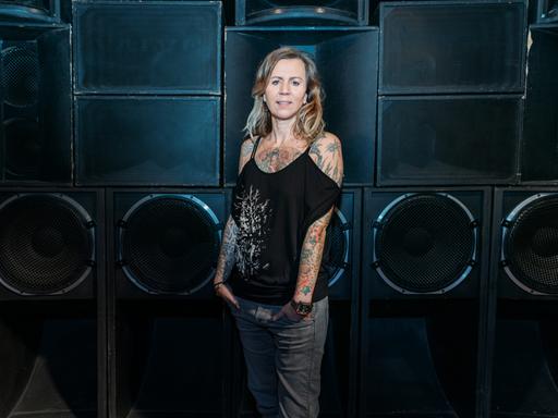 Pamela Schobeß, Clubbetreiberin und Vorsitzende der Clubcommission Berlin, steht vor einer Wand aus riesigen Lautsprechern.
