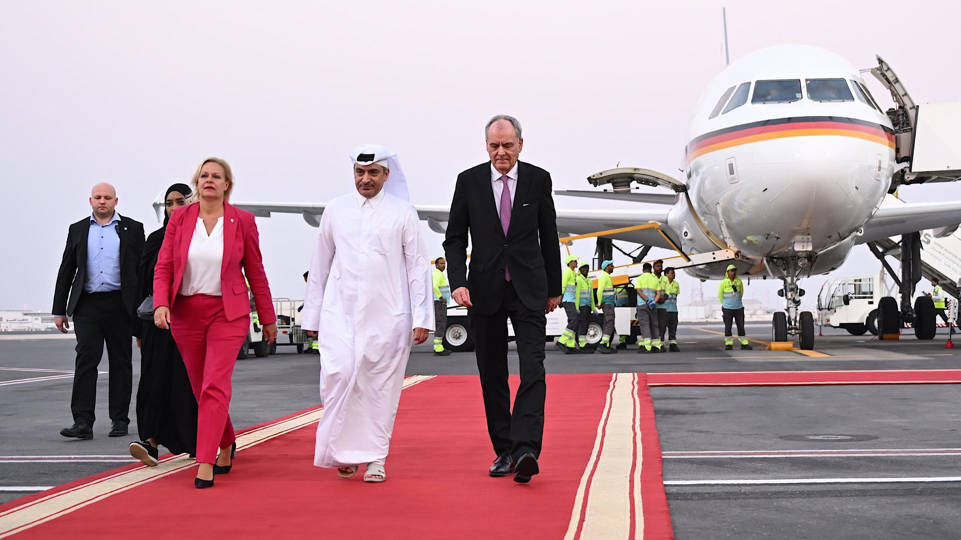 Ministerin Nancy Faeser  wird am Flughafen von der Stadt Doha in dem Land Katar empfangen. Sie trägt einen roten Anzug. 
