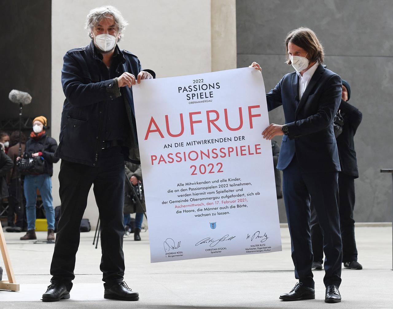 Zwei Männer halten ein Plakat in die Höhe, auf dem geschrieben steht: "2022 Passionsfestspiele. Aufruf an die Mitwirkenden an den den Passionsfestspiele 2022. Alle Mitwirkenden und alle KInder, die an den Passionsfestspielen 2022, werden hiermit vom Spielleiter und der Gemeinde Oberammergau aufgefordert, sich ab dem Aschermittwoch , den 17. Februar 202q, die Haare, de Männer auch die Bärte, wachsen zu lassen." Darunter sind drei Unterschriften zu sehen. Zwei Männer halten ein Plakat in die Höhe, auf dem geschrieben steht: "2022 Passionsfestspiele. Aufruf an die Mitwirkenden an den den Passionsfestspiele 2022. Alle Mitwirkenden und alle KInder, die an den Passionsfestspielen 2022, werden hiermit vom Spielleiter und der Gemeinde Oberammergau aufgefordert, sich ab dem Aschermittwoch , den 17. Februar 202q, die Haare, de Männer auch die Bärte, wachsen zu lassen." Darunter sind drei Unterschriften zu sehen.