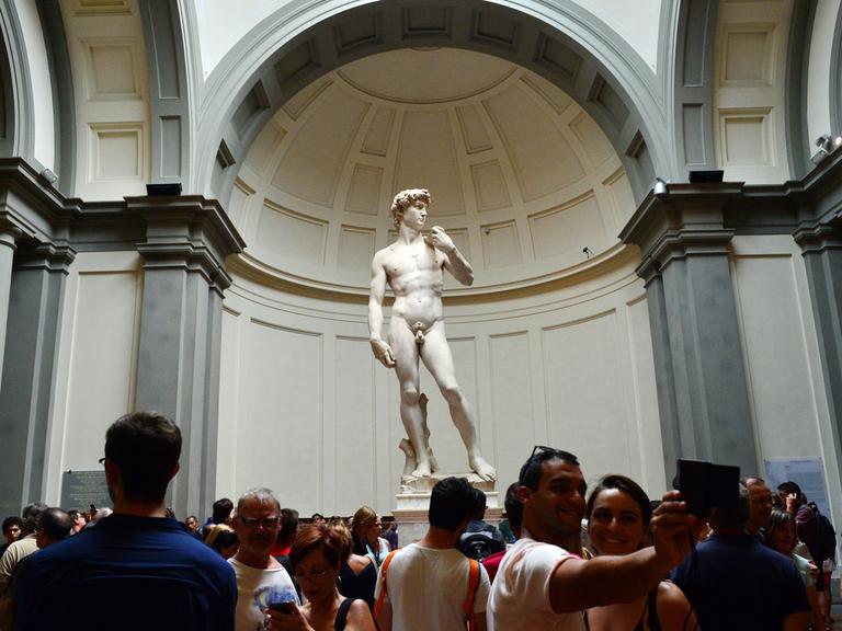 Der David von Michelangelo in der Galleria dell Accademia in Florenz. Vor der Statue stehen viele Besucher, einige machen mit ihren Handys Fotos.