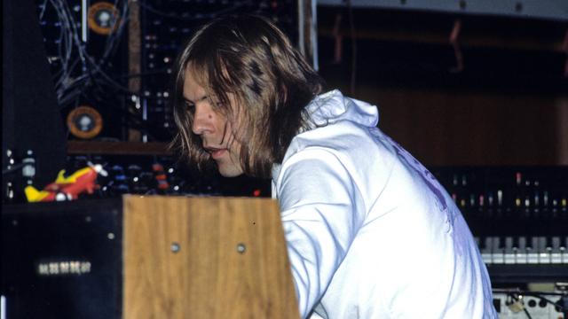 Klaus Schulze sitzt im weißen Pulli auf der Bühne und spielt an einem Synthesizer mit Holzverkleidung.