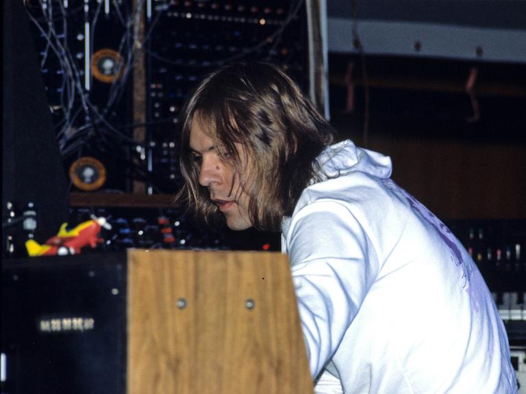 Klaus Schulze sitzt im weißen Pulli auf der Bühne und spielt an einem Synthesizer mit Holzverkleidung.