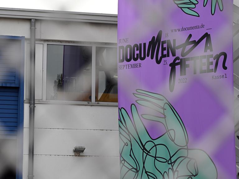 Das Logo der Documenta 15 ist vor einem Ausstellungsgebäude angebracht. Es ist ein lila Plakat mit schwarzer Schrift.