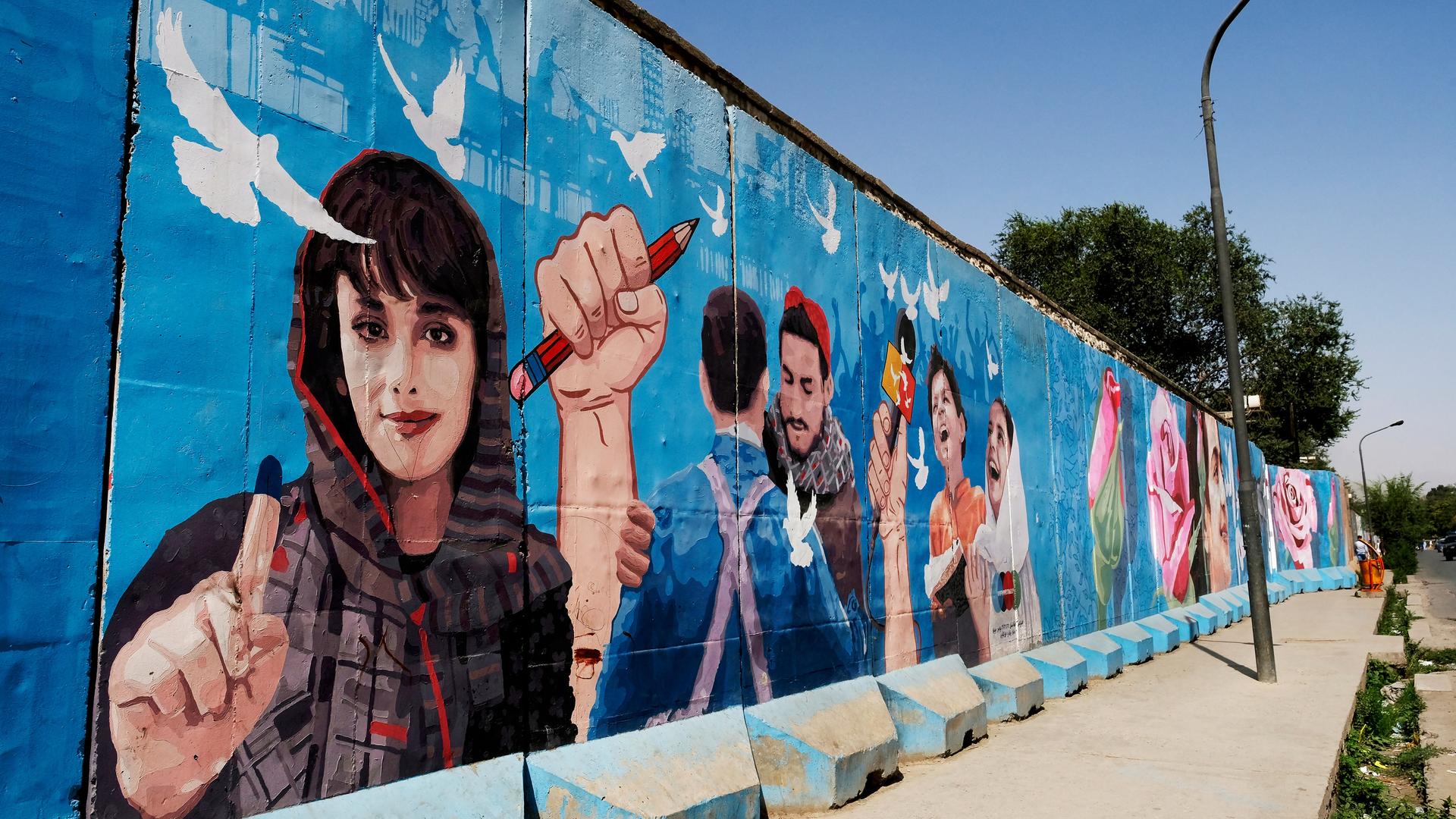 Auf einer bemalten Mauer in Kabul sind Friedenstauben sowie verschiedene Personen zu sehen, darunter eine Frau mit erhobenem Zeigefinger.