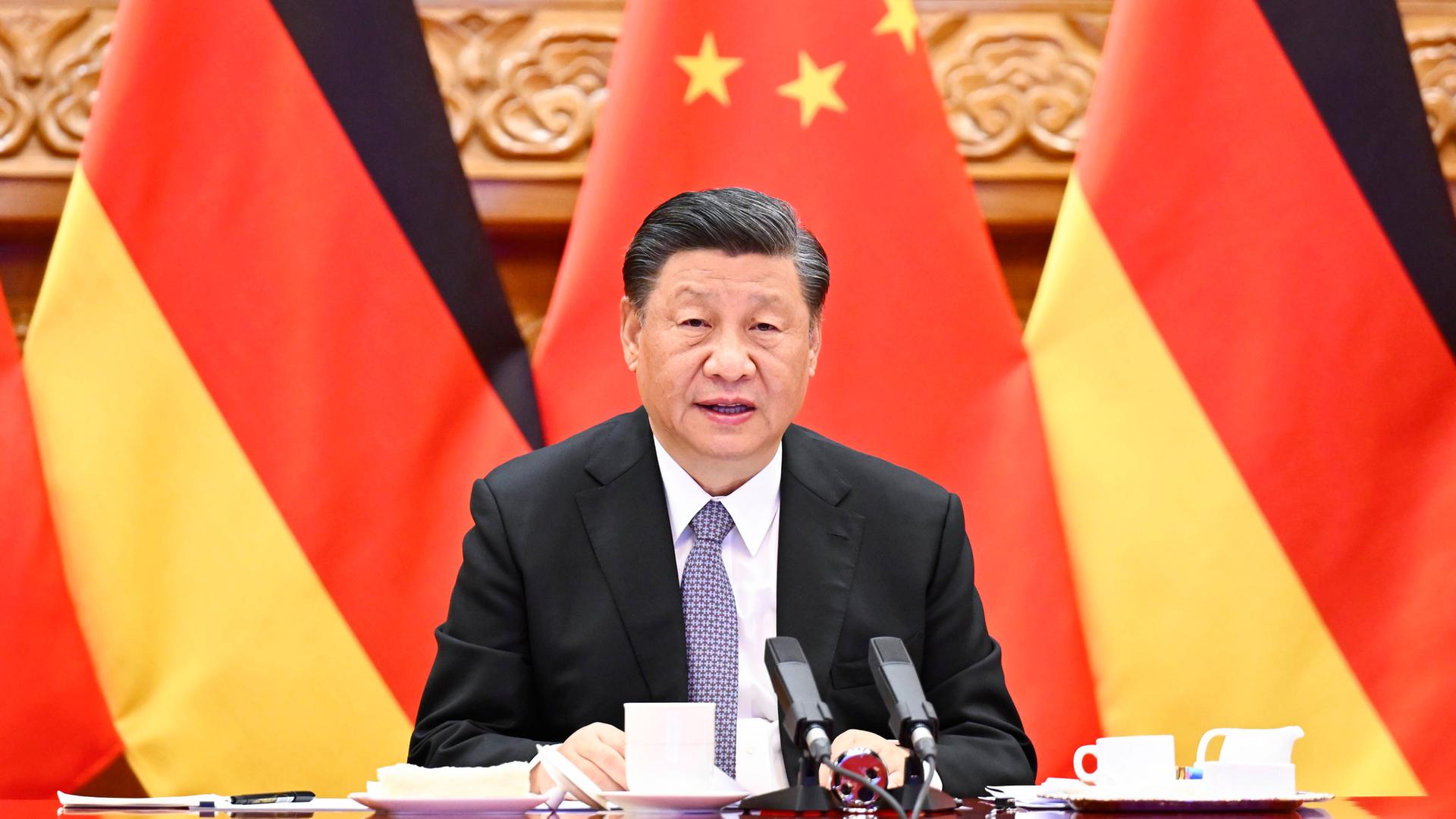 Xi Jinping sitzt vor deutschen und chinesischen Fahnen Xi Jinping sitzt vor deutschen und chinesischen Fahnen