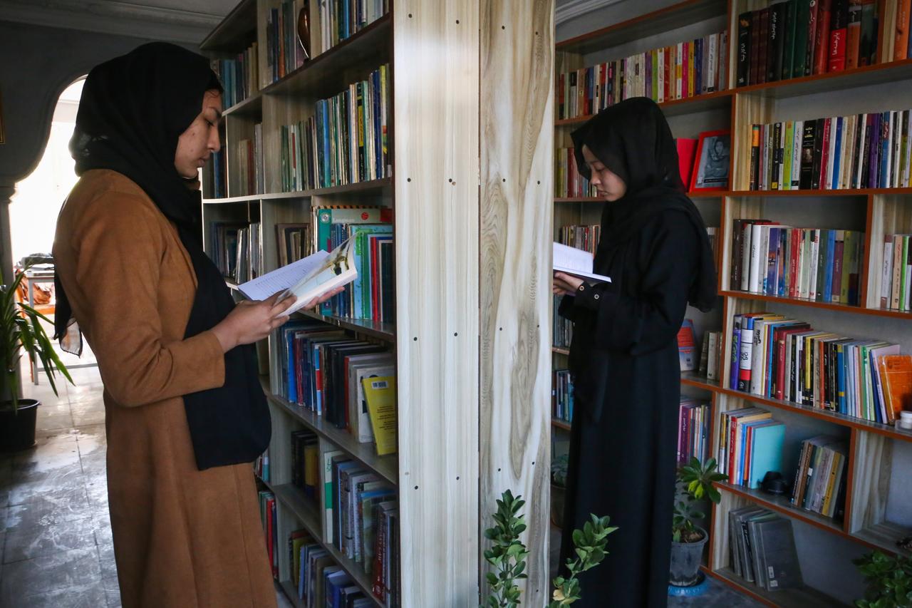 Lesende afghanische Mädchen in Kopftuch und langen Gewändern in einer Bibliothek in Kabul Lesende afghanische Mädchen in Kopftuch und langen Gewändern in einer Bibliothek in Kabul