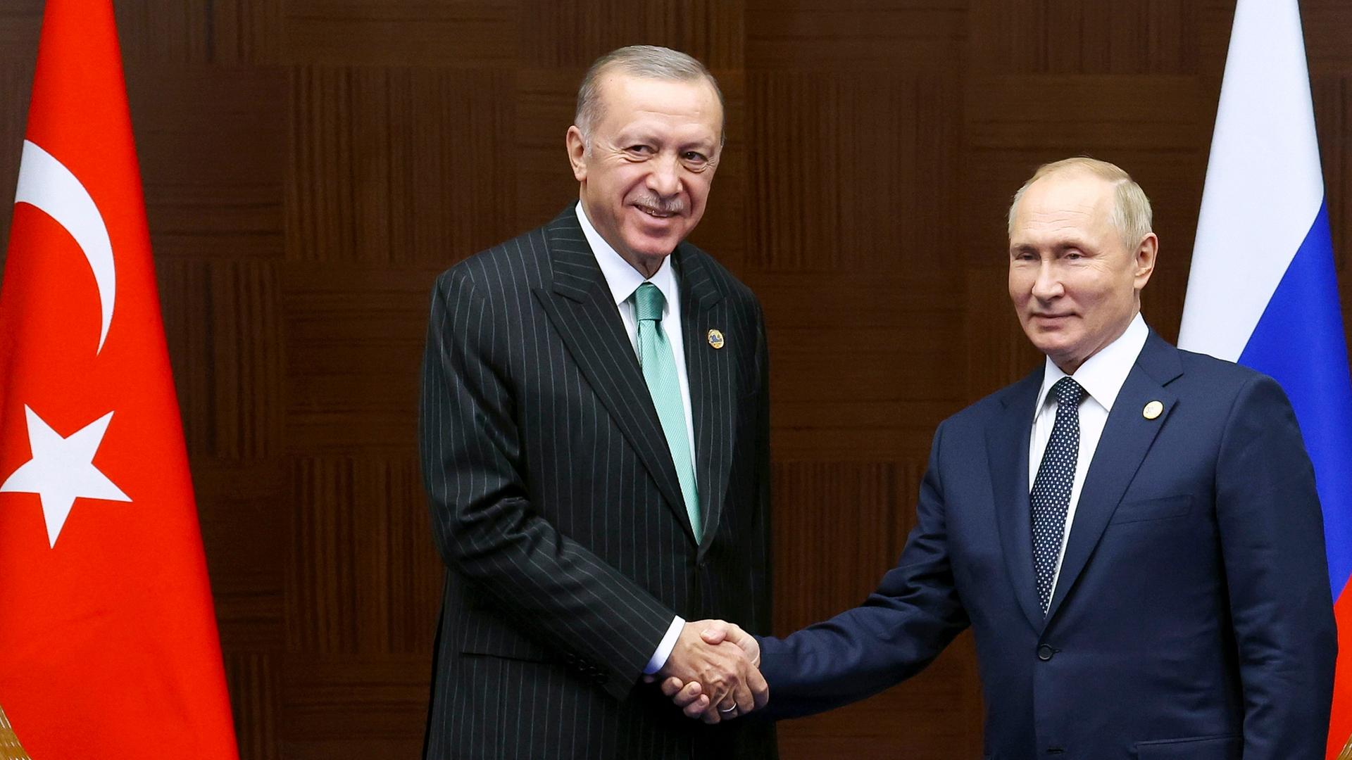 Der türkische Präsident Erdogan (l.) gibt  Russlands Staatschef Putin die Hand, dahinter die Flaggen der beiden Länder.