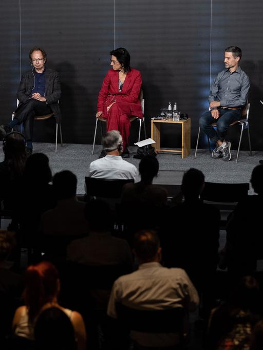 Zwei Frauen und vier Männer sitzen bei einer Podiumsdiskussion vor Publikum auf einer Bühne.