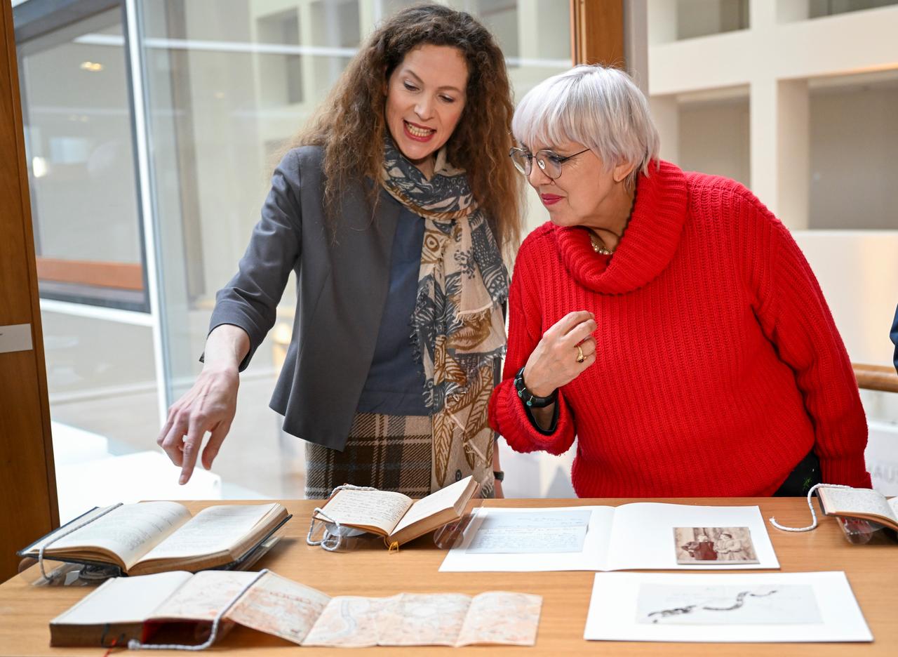 Sandra Richter, die Direktorin des Deutschen Literaturarchivs Marbach zeigt mit einem Finger auf ein Buch in einer Glasvitirine. Neben ihr Kulturstaatsministerin Claudia Roth (Bündnis 90/Die Grünen). Sandra Richter, die Direktorin des Deutschen Literaturarchivs Marbach zeigt mit einem Finger auf ein Buch in einer Glasvitirine. Neben ihr Kulturstaatsministerin Claudia Roth (Bündnis 90/Die Grünen).