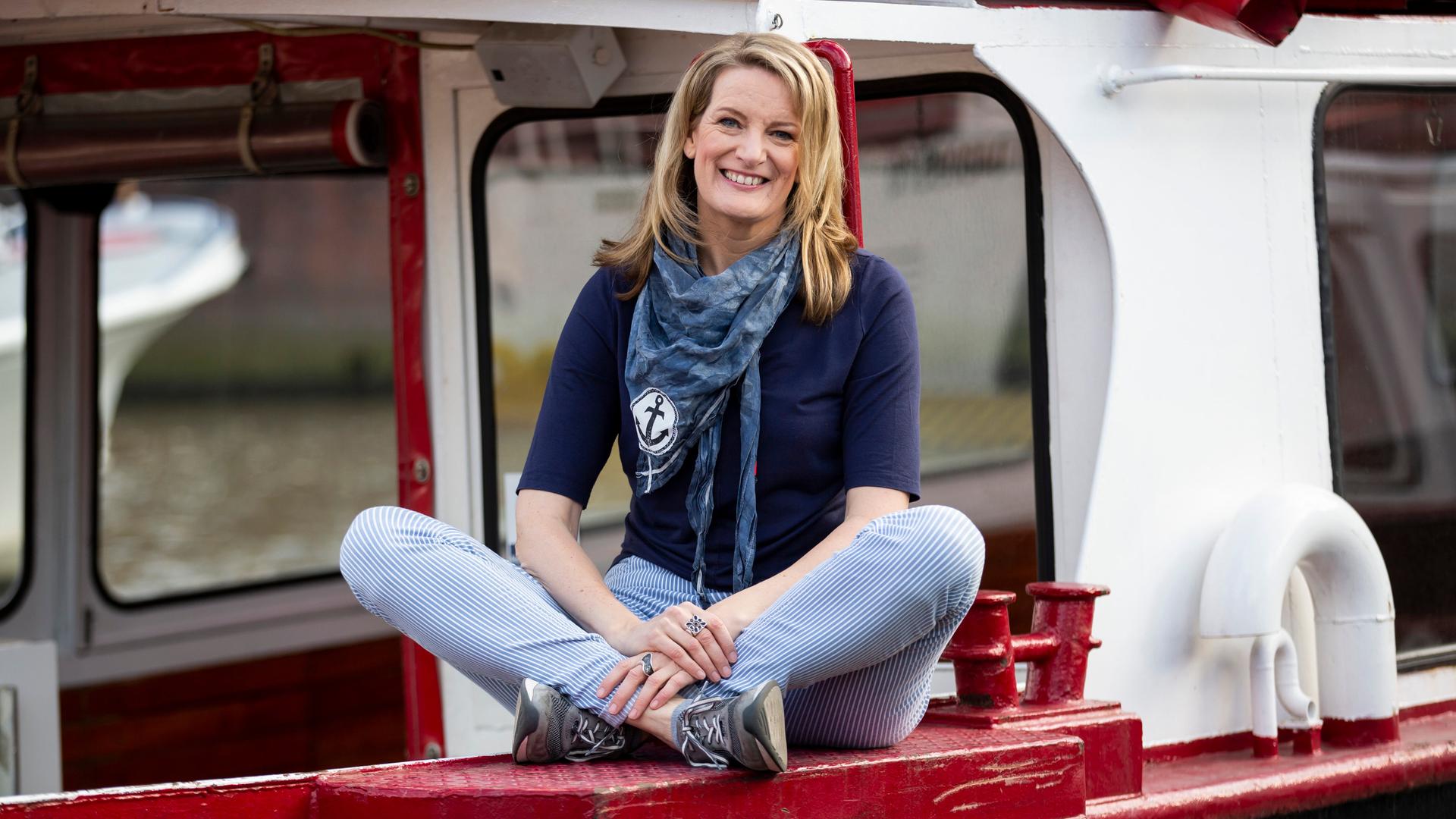 Tour-Guide Maike Brunk sitzt im Schneidersitz auf einer rotlackierten Fläche eines Schiffes. Tour-Guide Maike Brunk sitzt im Schneidersitz auf einer rotlackierten Fläche eines Schiffes.