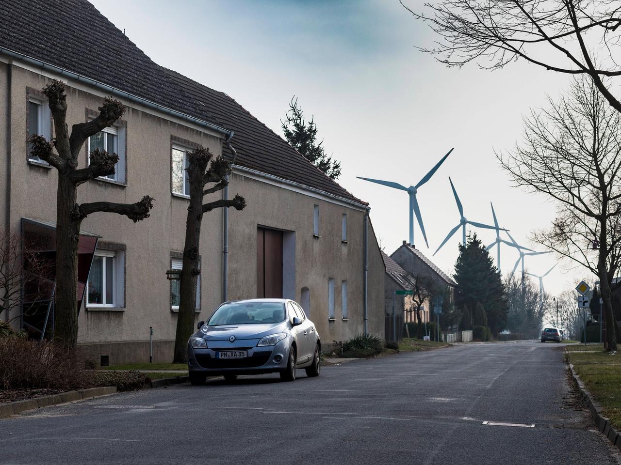 Eine Straße mit Wohnhäusern, Bäumen und einen Auto. Im Hintergrund sind mehrere Windkraftanlagen zu sehen. Es handelt sich um den Ort Feldheim im brandenburgischen Fläming, der sich selbst aus erneuerbarer Energie autark versorgt. Eine Straße mit Wohnhäusern, Bäumen und einen Auto. Im Hintergrund sind mehrere Windkraftanlagen zu sehen. Es handelt sich um den Ort Feldheim im brandenburgischen Fläming, der sich selbst aus erneuerbarer Energie autark versorgt.