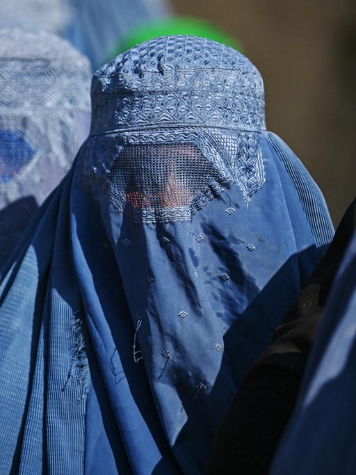 Eine Gruppe von vollverschleierten Frauen stehen hintereinander in einer Schlange.