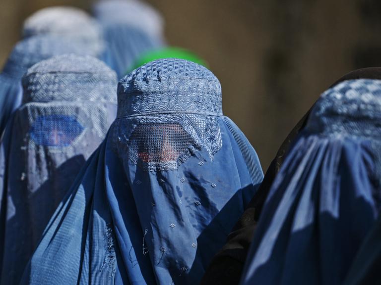 Eine Gruppe von vollverschleierten Frauen stehen hintereinander in einer Schlange.