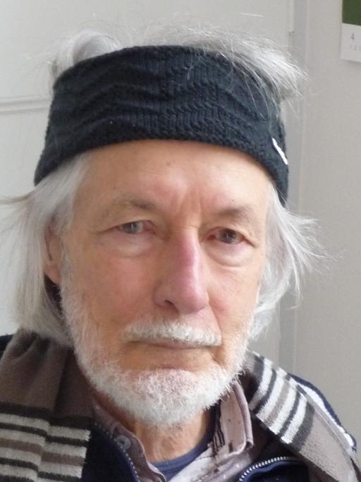Ein älterer Mann mit Bart grauen Haaren blickt mit Schal und Wollstirnband in die Kamera