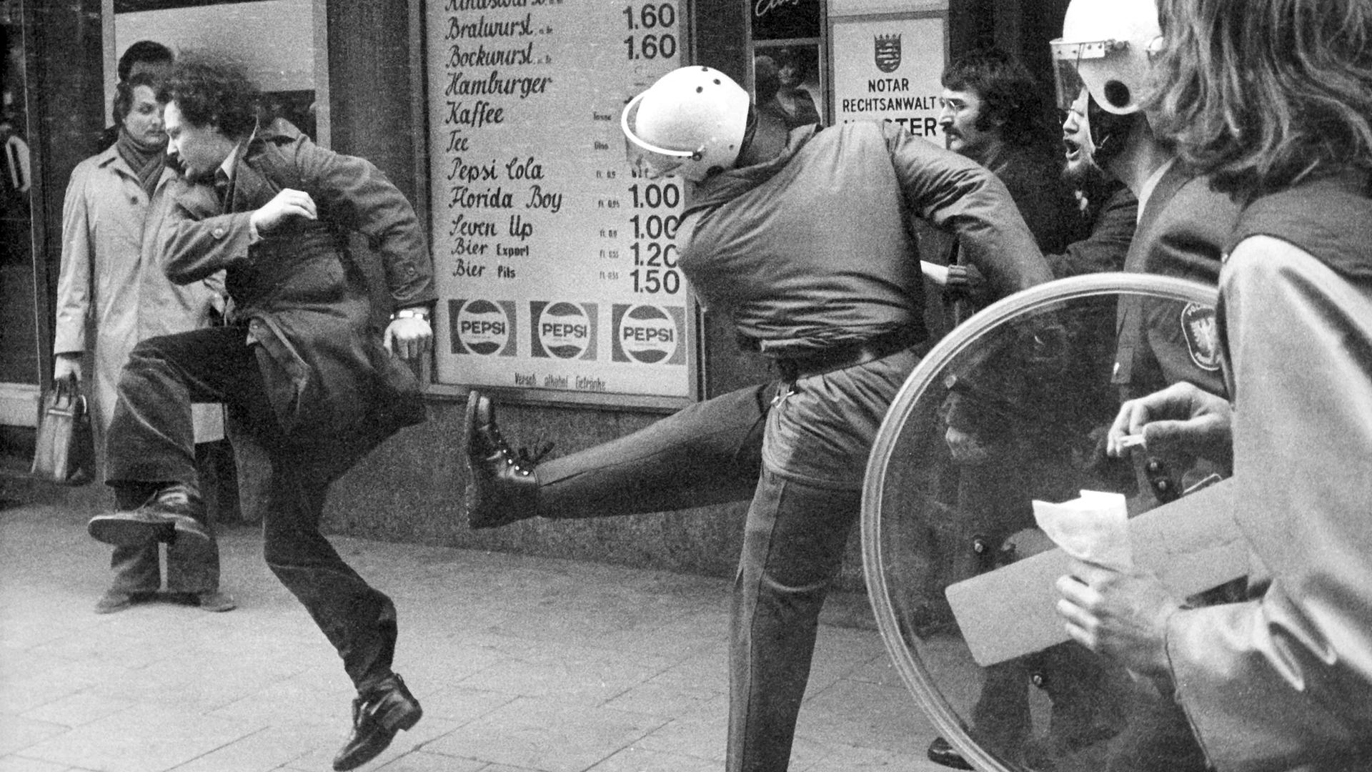 Martin gerät in eine Demonstration und wird zum Opfer polizeilicher Maßnahmen. Zu sehen: Polizeieinsatz  einer nicht genehmigten Demonstration 1974. Ein Polizist versucht, einem Demonstranten einen Tritt zu versetzen. 