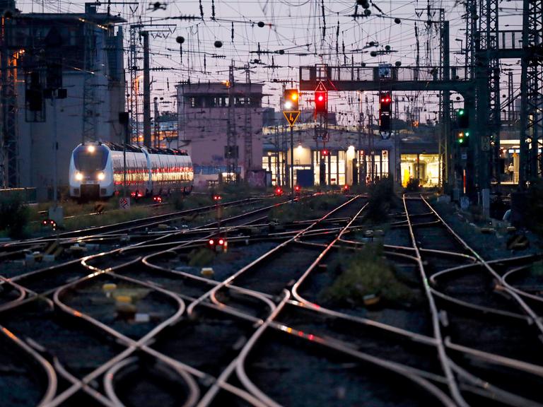 Verzweigte Eisenbahnschienen vor einem Bahnhof, links fährt ein ICE.