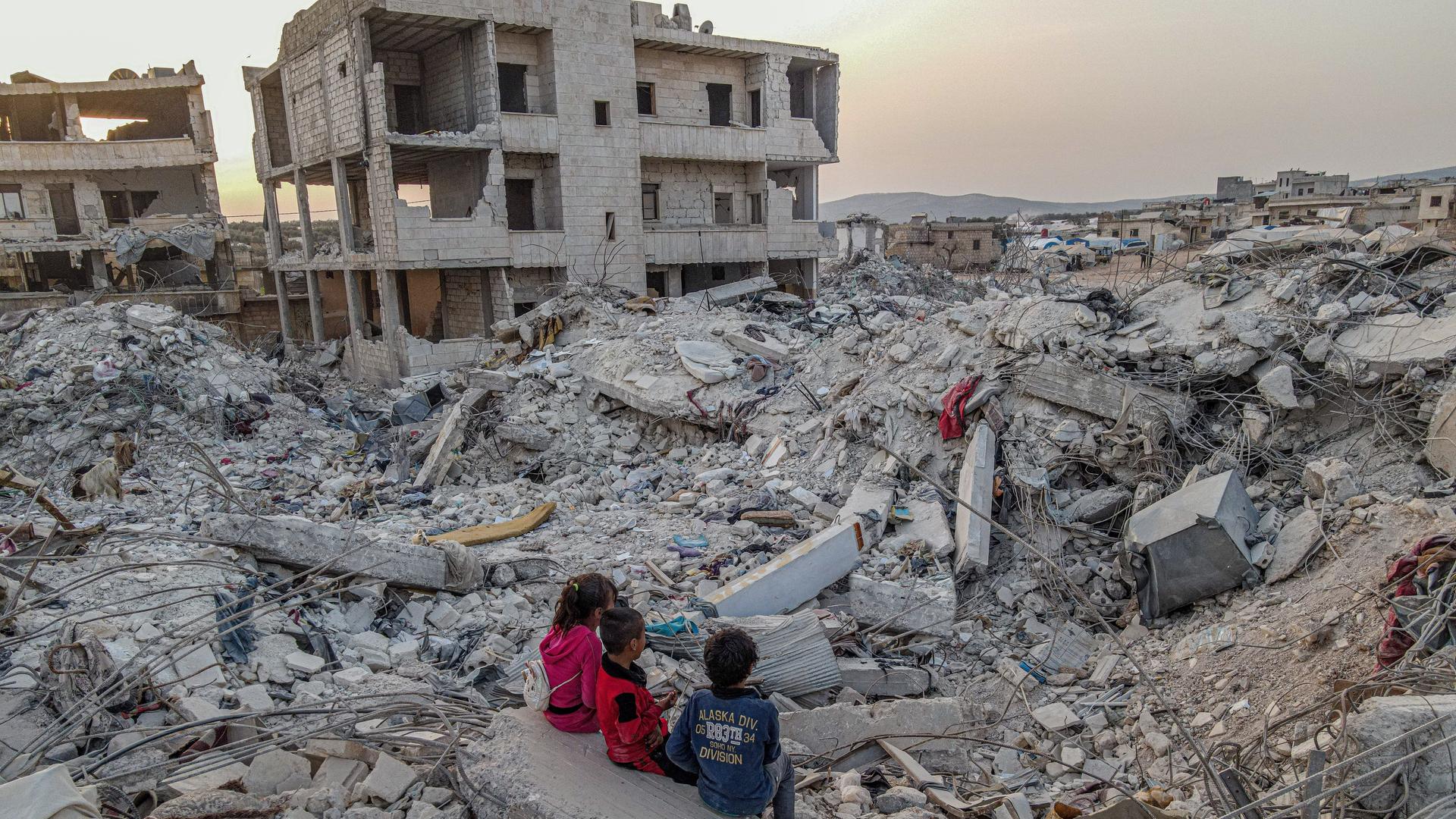 Drei Kinder sitzen in der syrischen Stadt Jenderes vor Gebäudetrümmern 