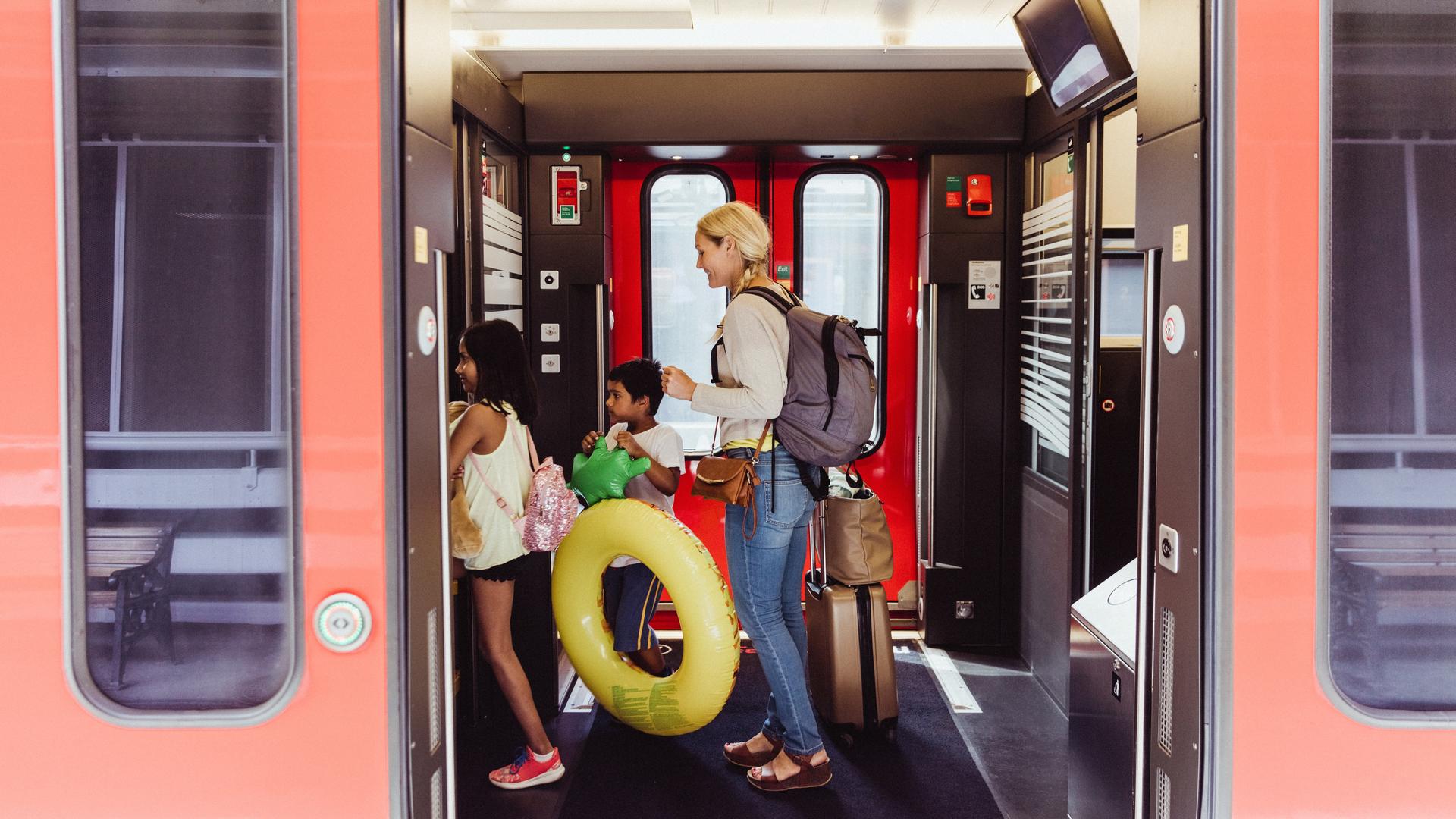 Eine Mutter und zwei Kinder mit Schwimmreifen und Wasserspielzeug steigen in eine Bahn ein. Eine Mutter und zwei Kinder mit Schwimmreifen und Wasserspielzeug steigen in eine Bahn ein.