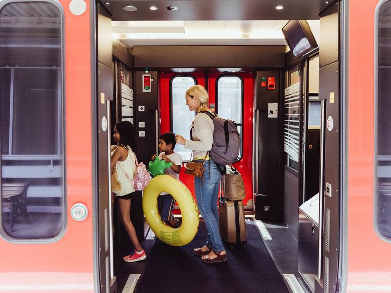 Eine Mutter und zwei Kinder mit Schwimmreifen und Wasserspielzeug steigen in eine Bahn ein.