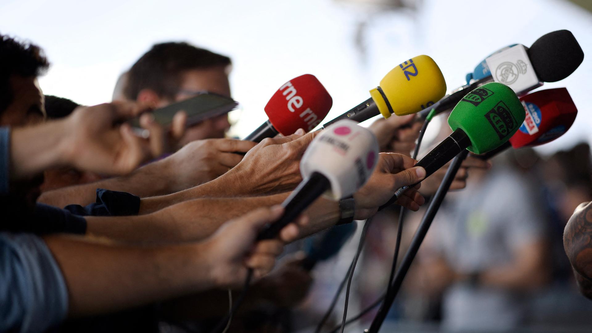 Journalisten halten ihre Mikrofone in Richtung eines Redners. Journalisten halten ihre Mikrofone in Richtung eines Redners.