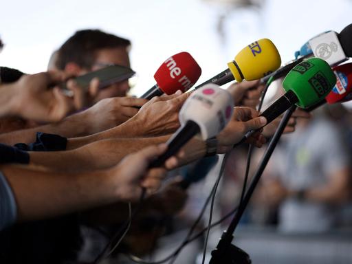Journalisten halten ihre Mikrofone in Richtung eines Redners.