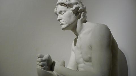 Eine weiße Skulptur, weitlich abgelichtet, von Ludwig van Beethoven als Abguss von Max Klingers Werk aus dem Jahr 1900, wobei er mit freiem Oberkörper und geballter Faust auf einem Stein sitzt und sich leicht nach vorn beugt.