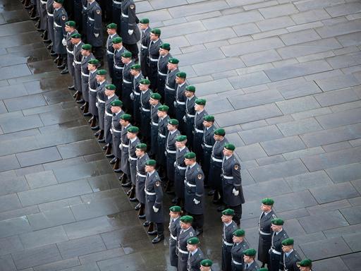 Drei Reihen von Soldaten eines Wachbataillons stehen auf grauem Pflaster.
