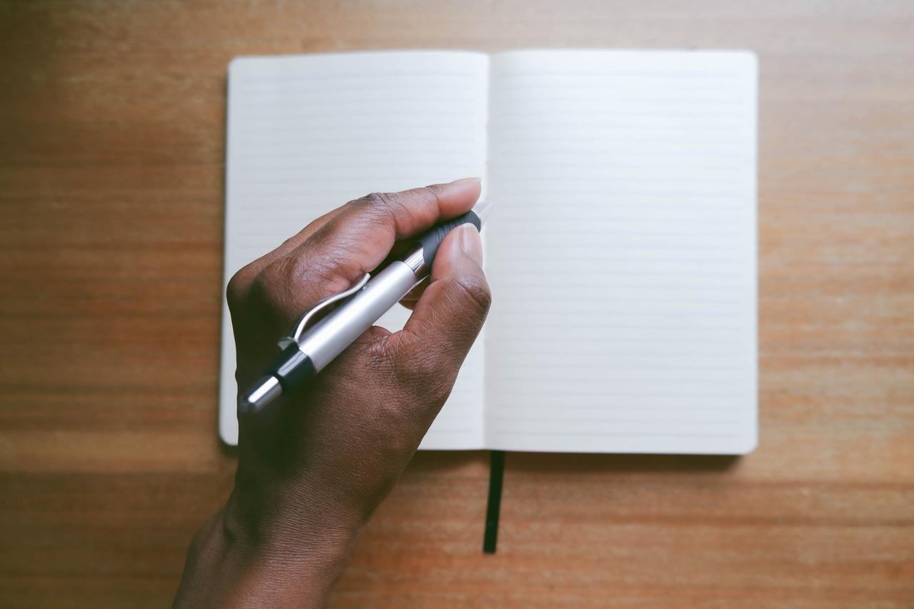 Nahaufnahme einer nicht erkennbaren Frau, die mit der linken Hand in ein Notizbuch schreibt. Nahaufnahme einer nicht erkennbaren Frau, die mit der linken Hand in ein Notizbuch schreibt.