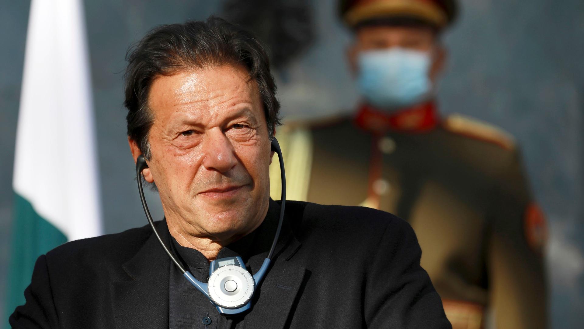 Der frühere pakistanische Premierminister Imran Khan hat Köpfhörer an und hört einer Übersetzung zu. Im Hintergund verschwommen ein Polizist.