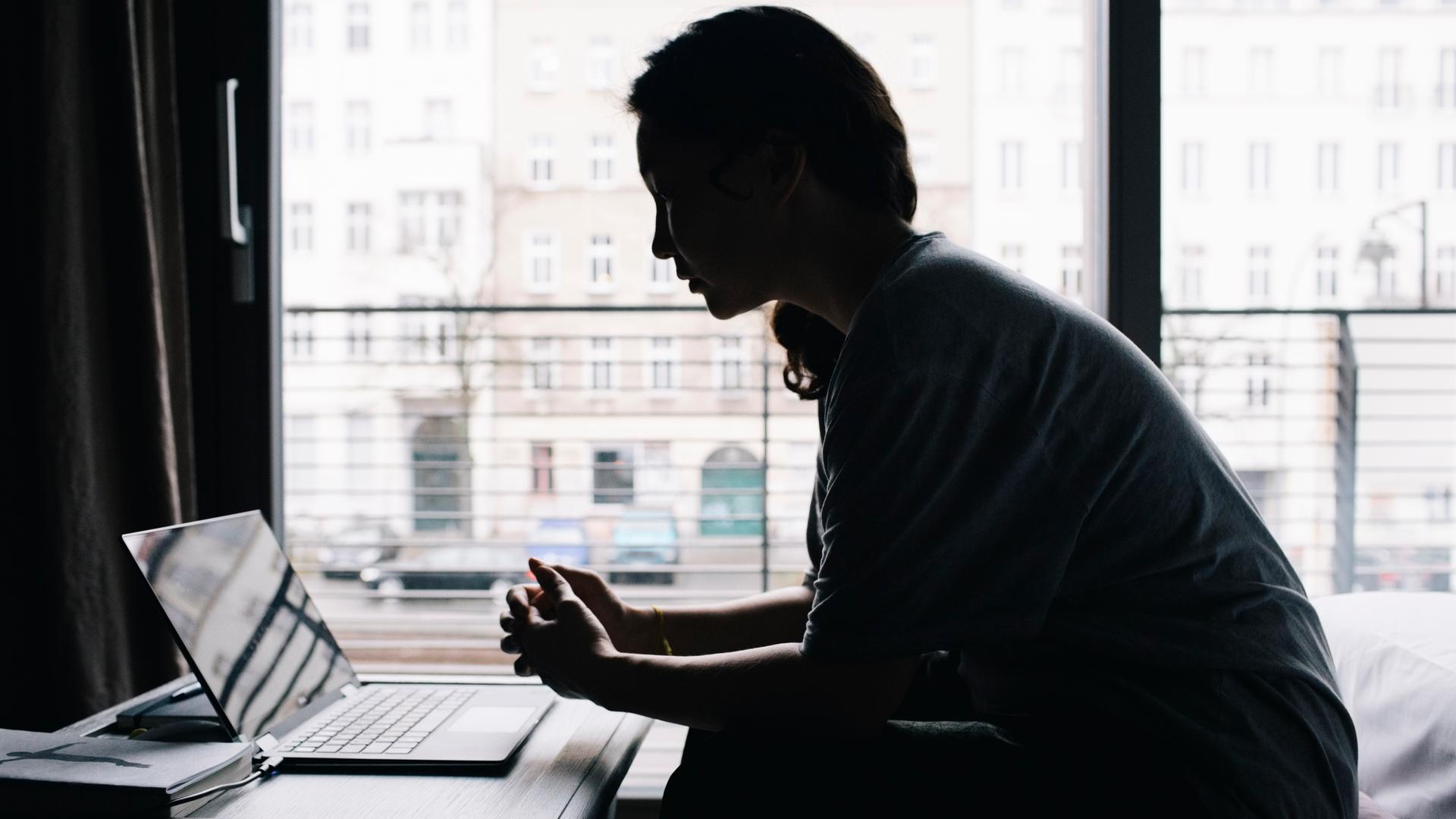 Eine junge Frau sitzt vor dem Fenster am Laptop. Eine junge Frau sitzt vor dem Fenster am Laptop.
