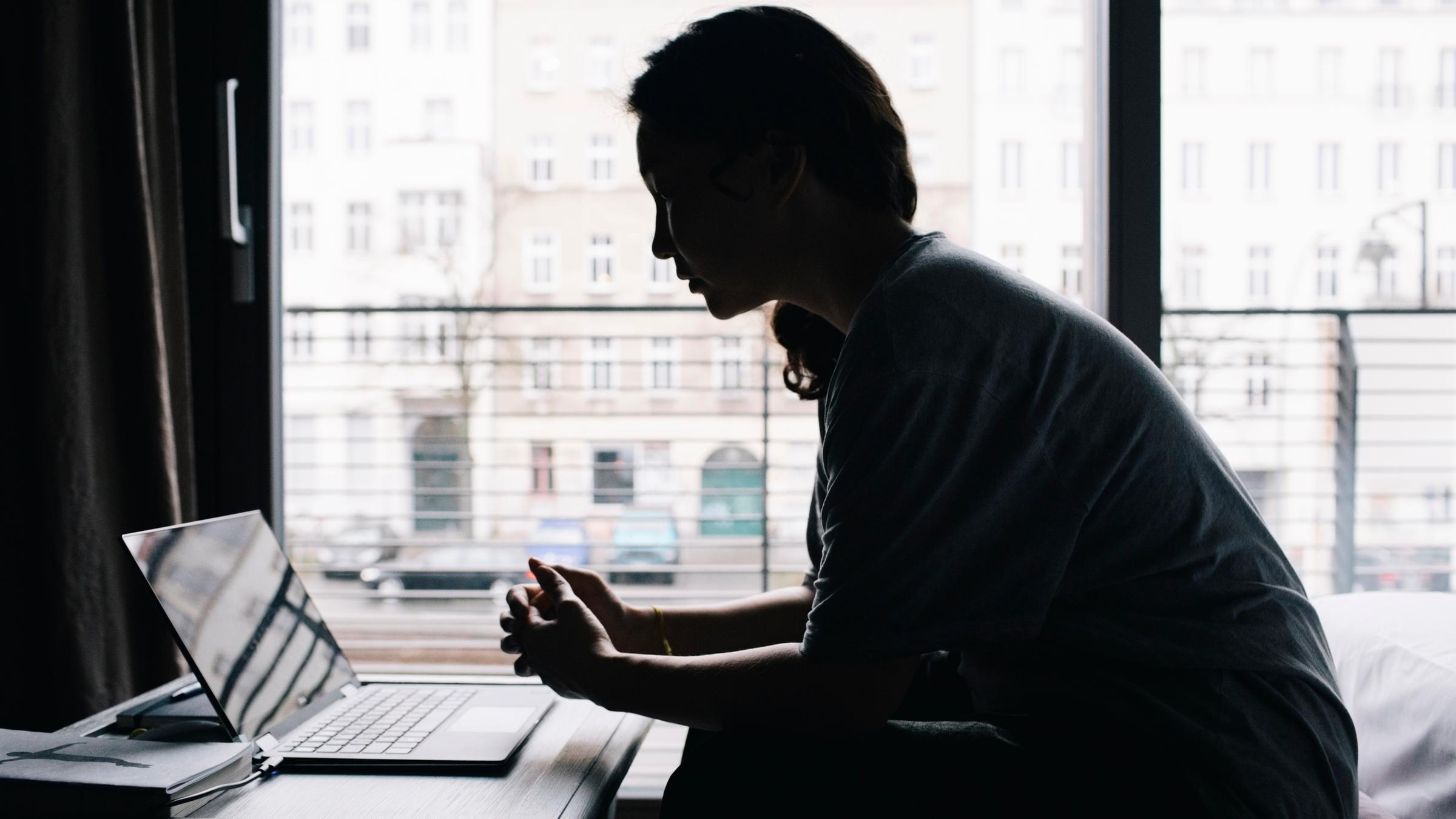 Eine junge Frau sitzt vor dem Fenster am Laptop. 