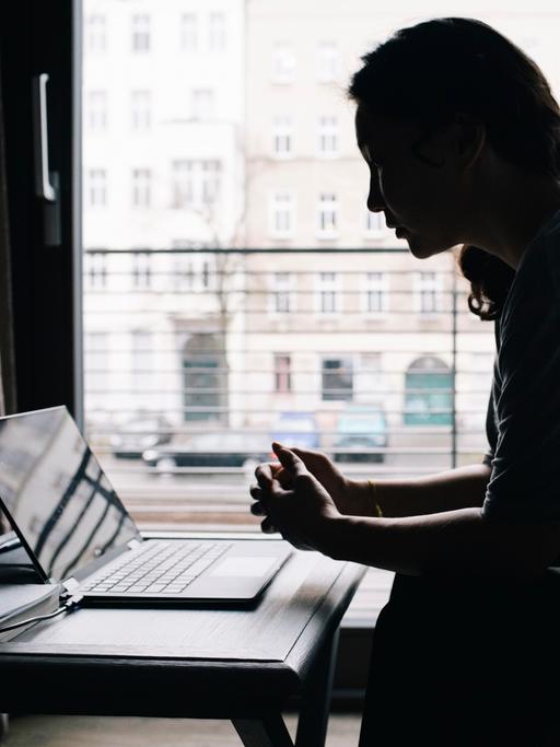 Eine junge Frau sitzt vor dem Fenster am Laptop. 