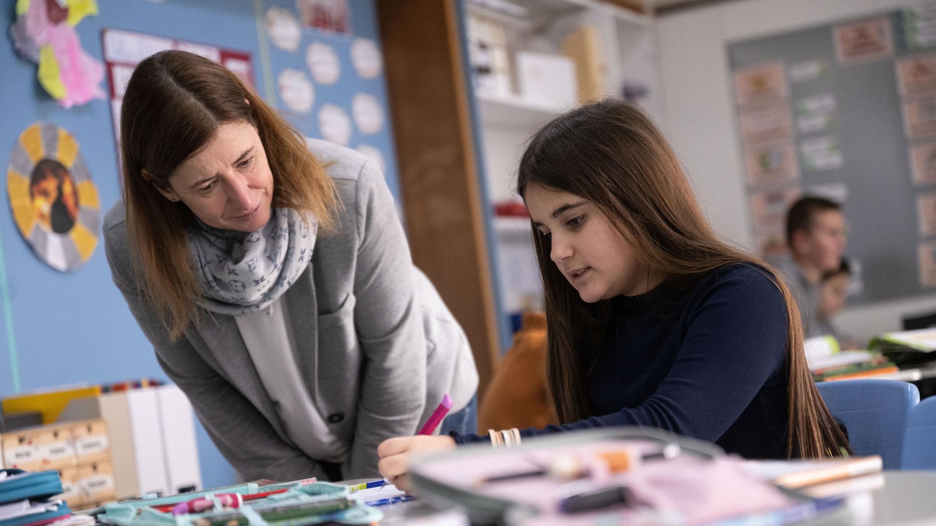 Eine Lehrerin guckt auf den Tisch von einer Schülerin und spricht mit ihr. Eine Lehrerin guckt auf den Tisch von einer Schülerin und spricht mit ihr.