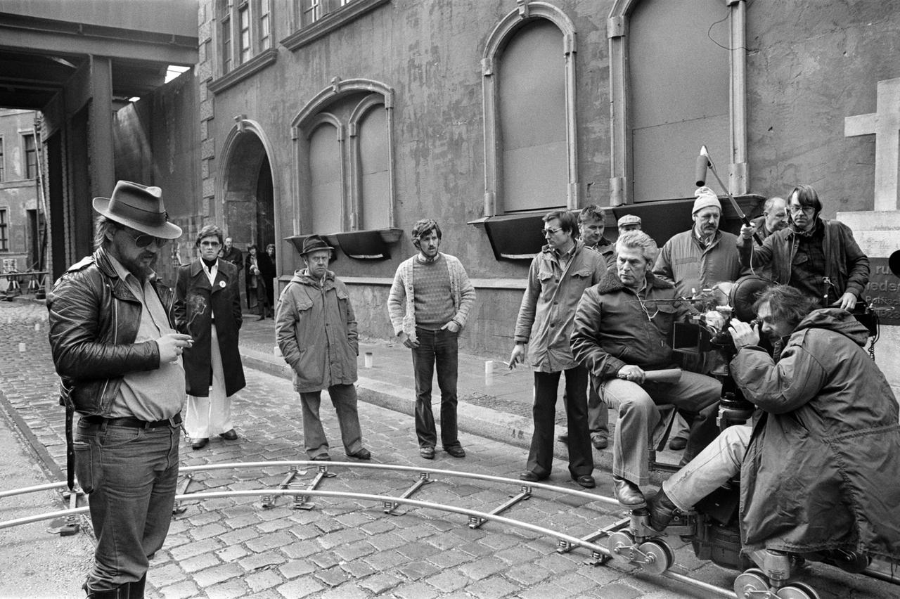 Rainer Werner Fassbinder steht rauchend vor einer Kamera-Dolly.