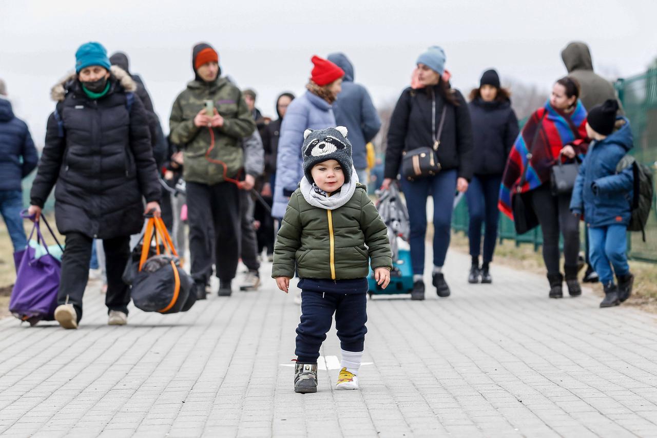 Familien mit Gepäck laufen auf einer Straße, im Vordergrund steht ein Kleinkind. Familien mit Gepäck laufen auf einer Straße, im Vordergrund steht ein Kleinkind.
