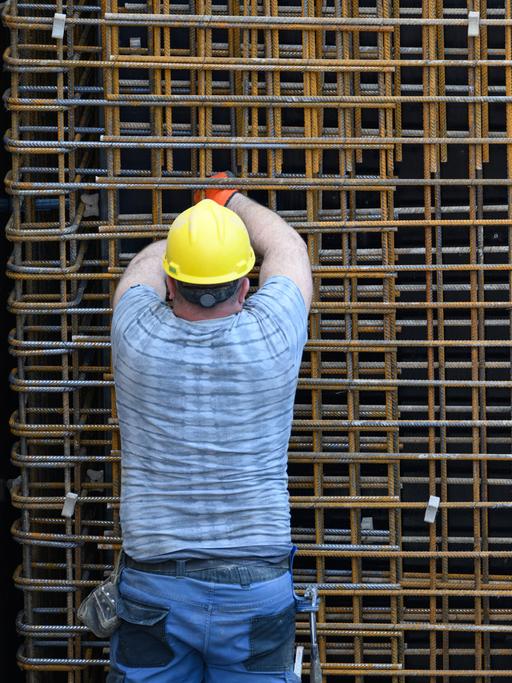 Ein Bauarbeiter mit Schutzkleidung und Helm steht auf einer Baustelle vor einem Metallgitter.