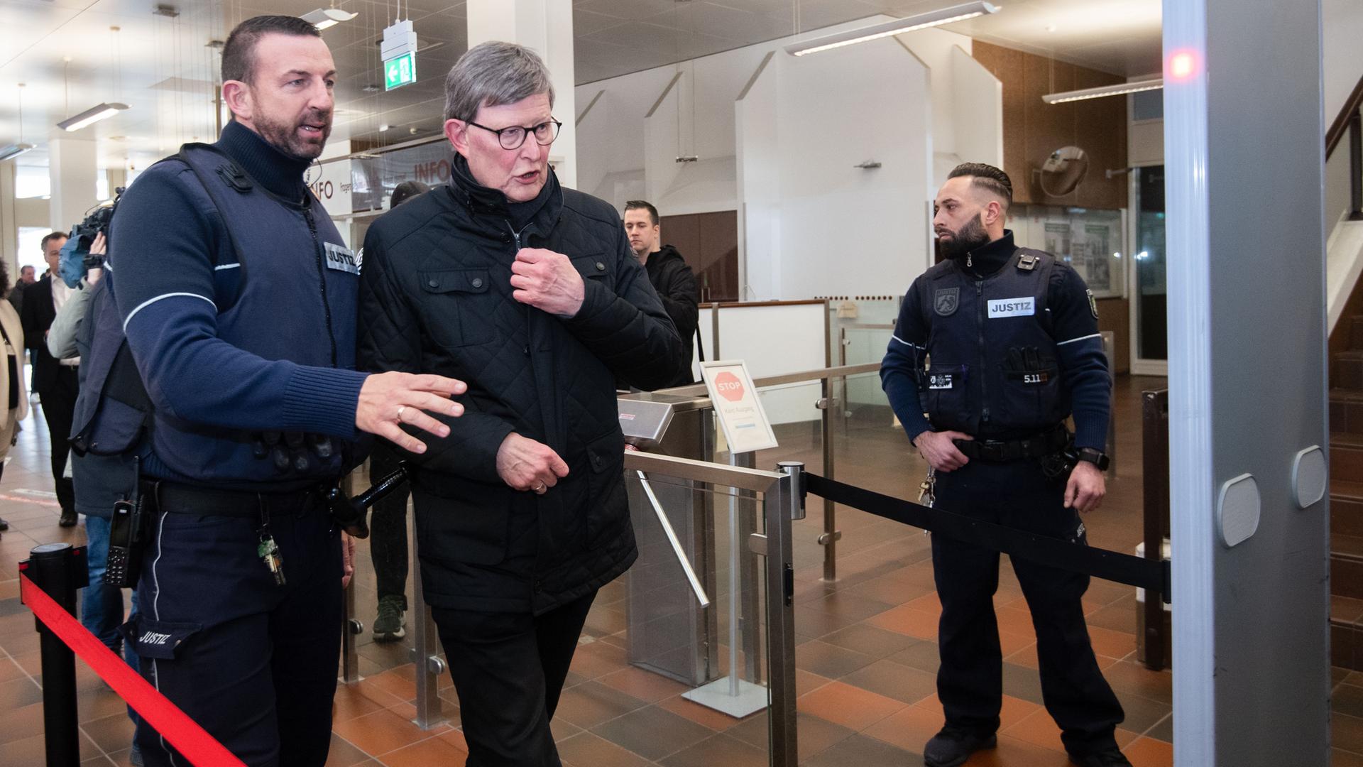 Köln: Kardinal Rainer Maria Woelki (2.v.l) wird im Foyer des Landgerichts von einem Justizbeamten zur Sicherheitsschleuse begleitet.